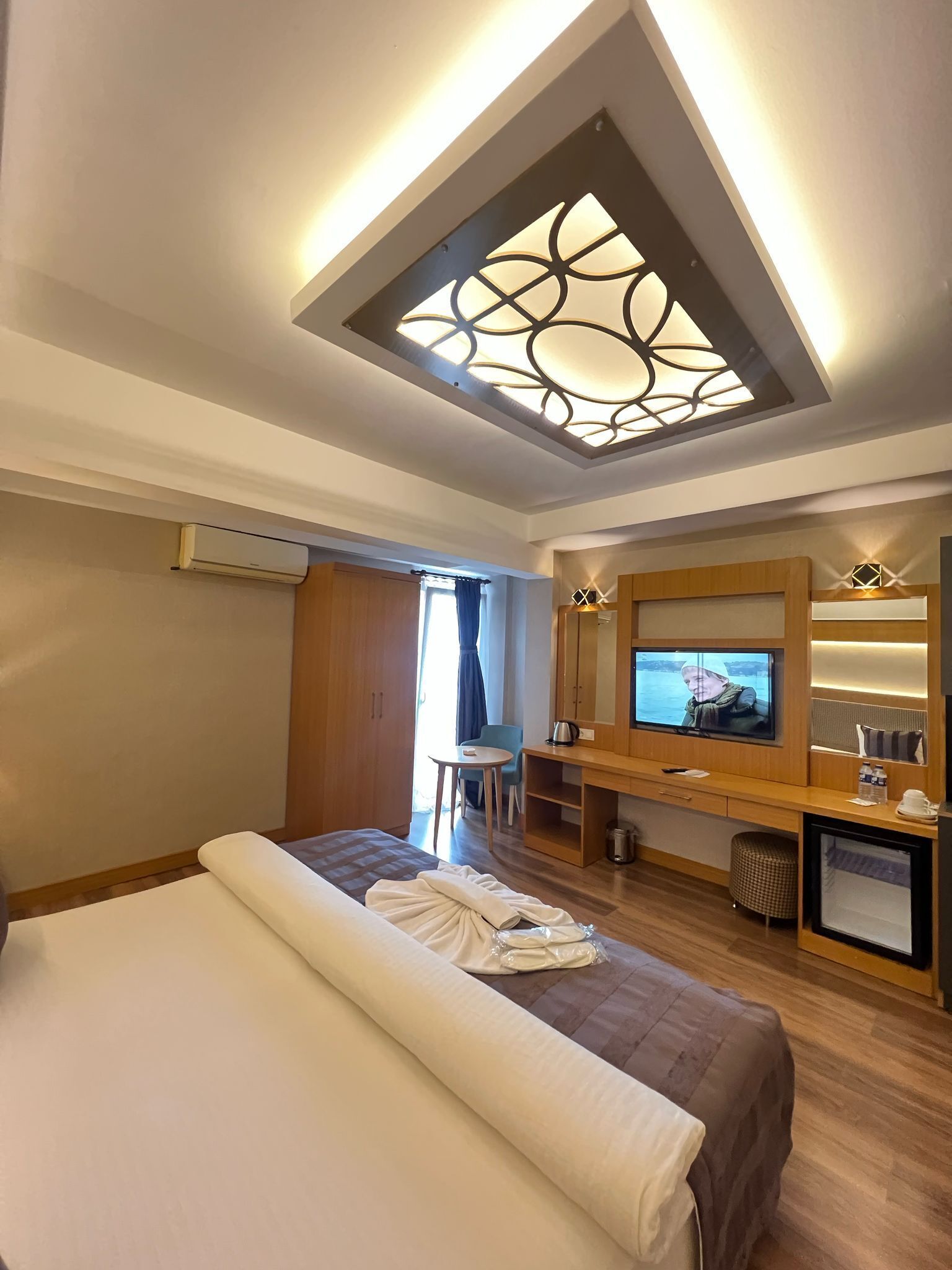 A hotel room with a bed, a desk, a TV, and a ceiling light fixture.