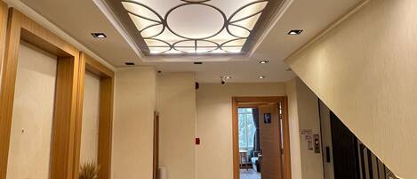 A hotel corridor with a modern ceiling design, a wooden table, and a staircase with a metal railing.
