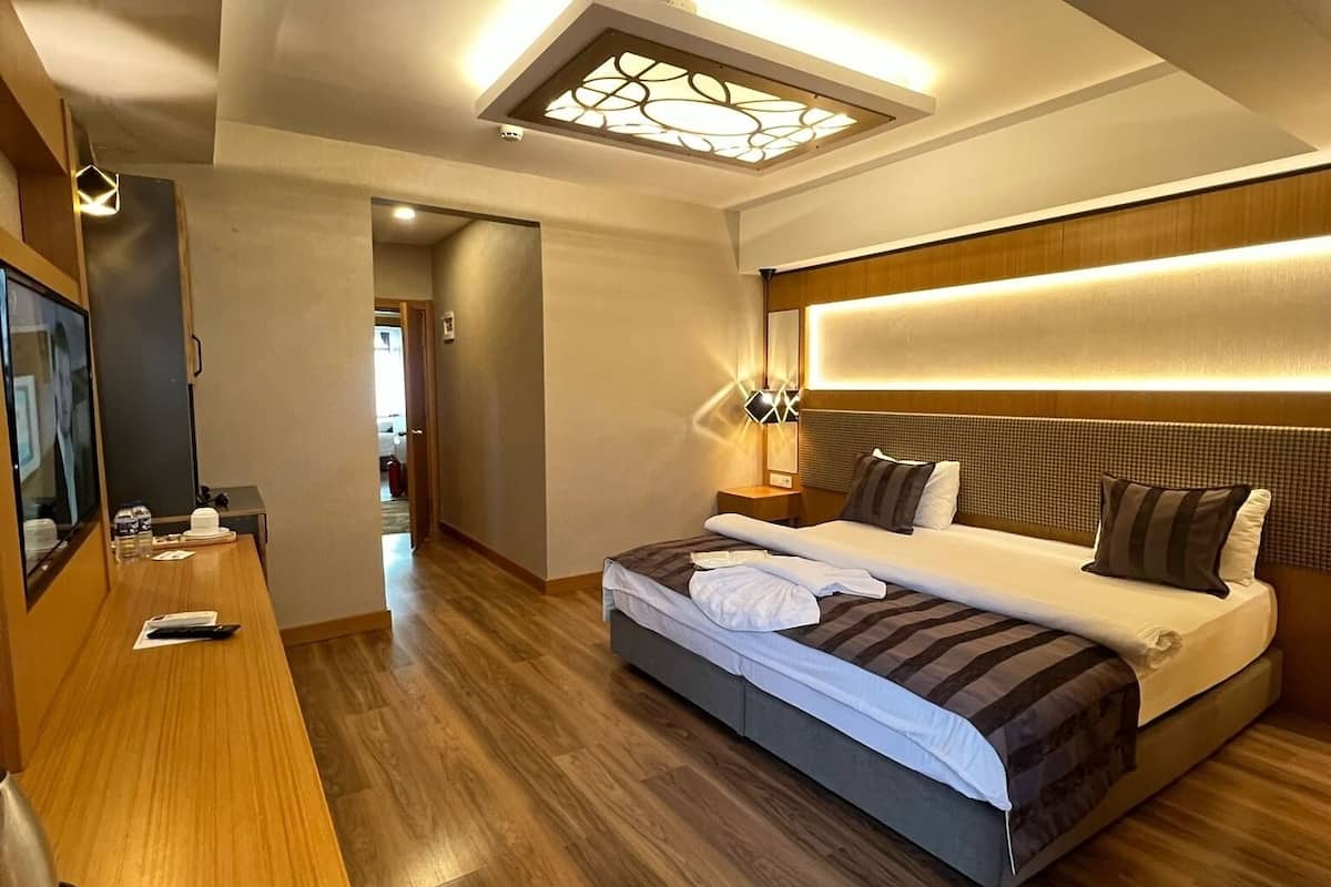 A hotel room with a large bed, a desk with a computer, a bedside lamp, and a ceiling light fixture.