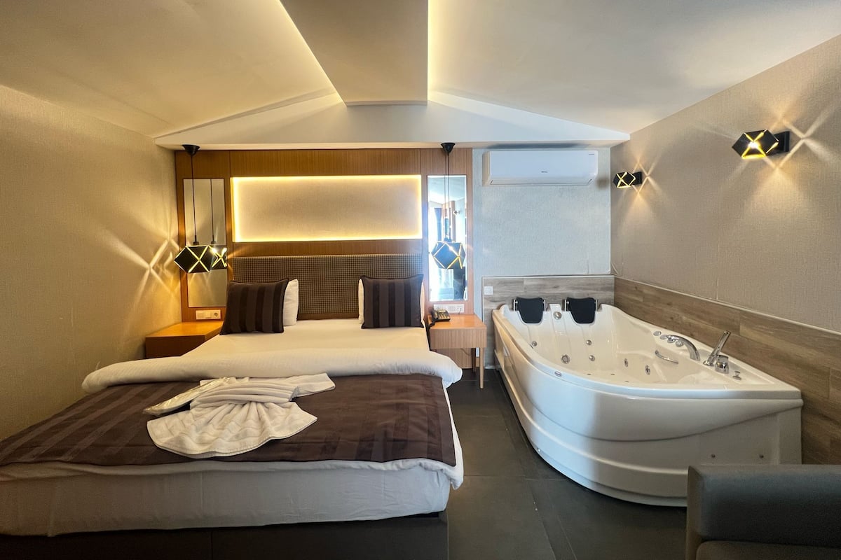 A modern hotel room with a large bed, a separate bathroom with a jacuzzi, and a large window.