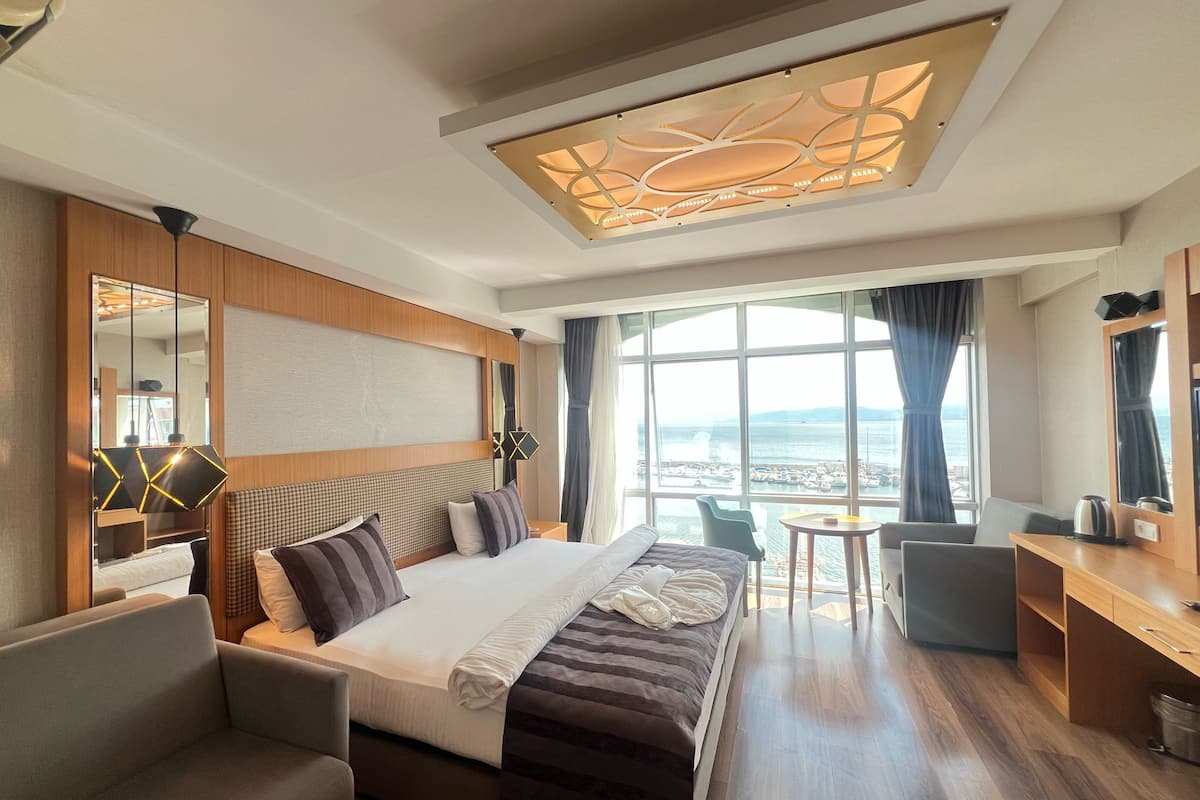 A hotel room with a large bed, a desk, a chair, and a view of the sea.