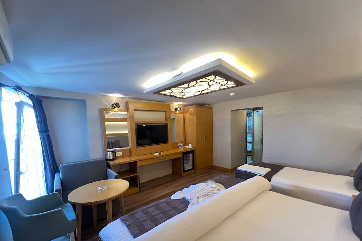 A hotel room with a bed, a desk with a TV, a chair, a small table, and a mirror.