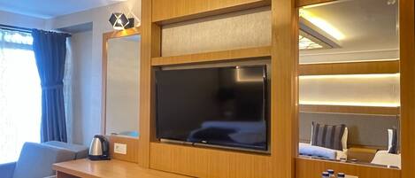 A hotel room with a wooden desk, a flat-screen TV, a coffee maker, and a minibar.