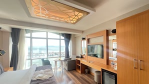 A hotel room with a bed, a TV, a small kitchenette, and a large window with a view of the sea. - The Port Rooms (Sinop)