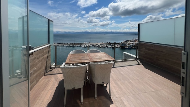 A balcony with a wooden table and two wicker chairs, overlooking a marina with boats and a clear sky. - The Port Rooms (Sinop)
