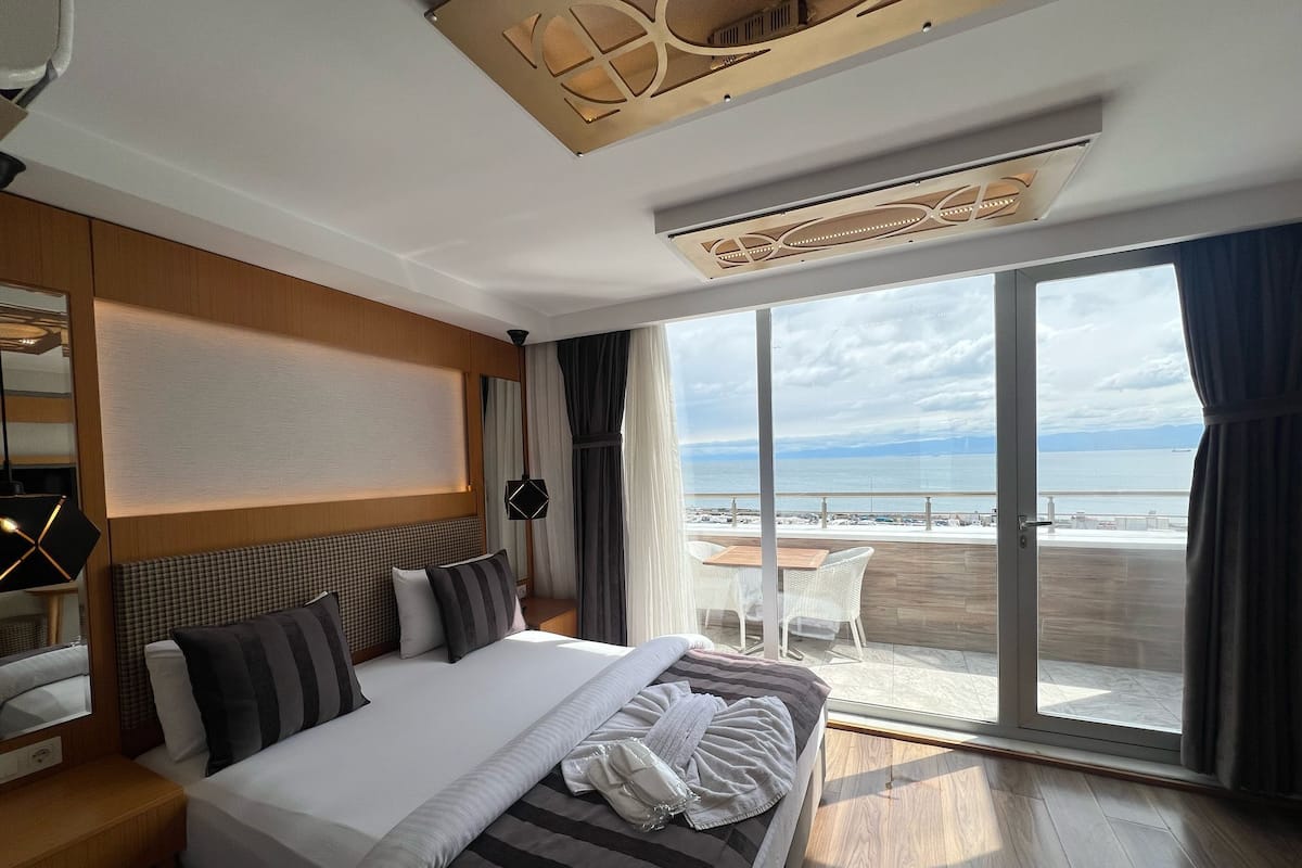 A hotel room with a large bed, a view of the beach, and a balcony with a table and chairs.