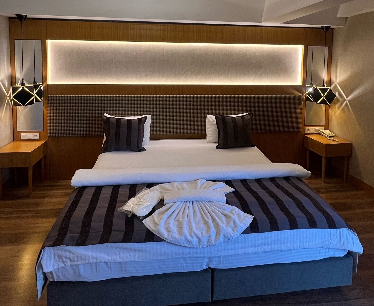 Une chambre d’hôtel moderne dotée d’un grand lit, de deux tables de chevet et d’une tête de lit avec éclairage intégré.