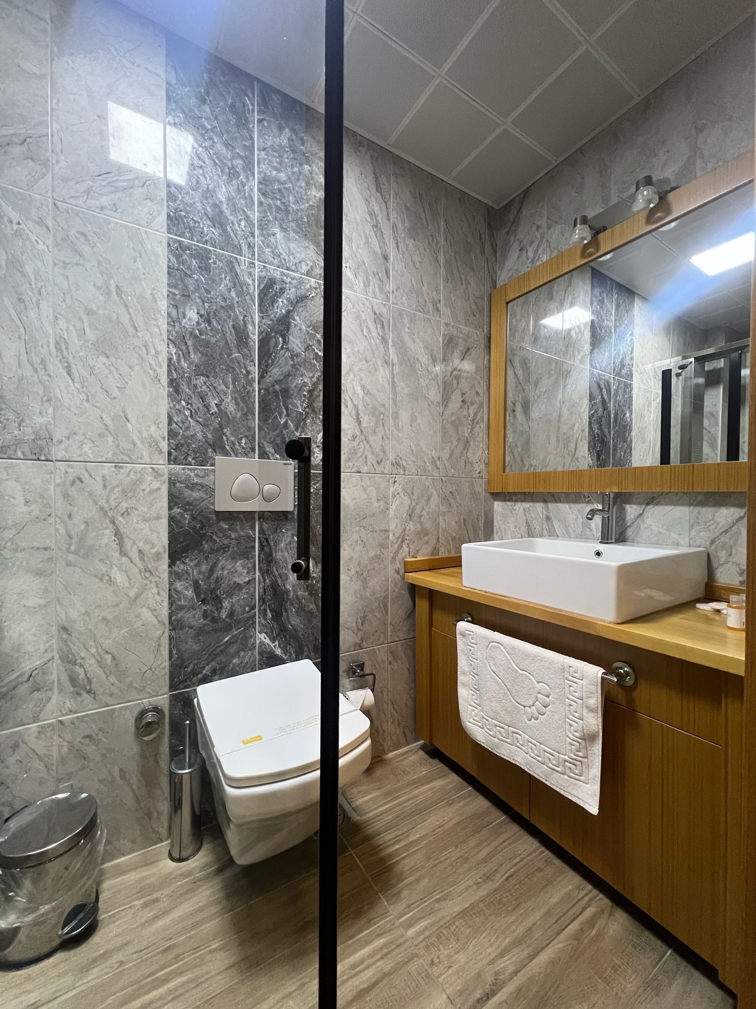 Un baño moderno con paredes de mármol, un tocador de madera, un lavabo blanco y un inodoro.