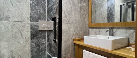 Un baño moderno con paredes de mármol, un tocador de madera, un lavabo blanco y un inodoro.