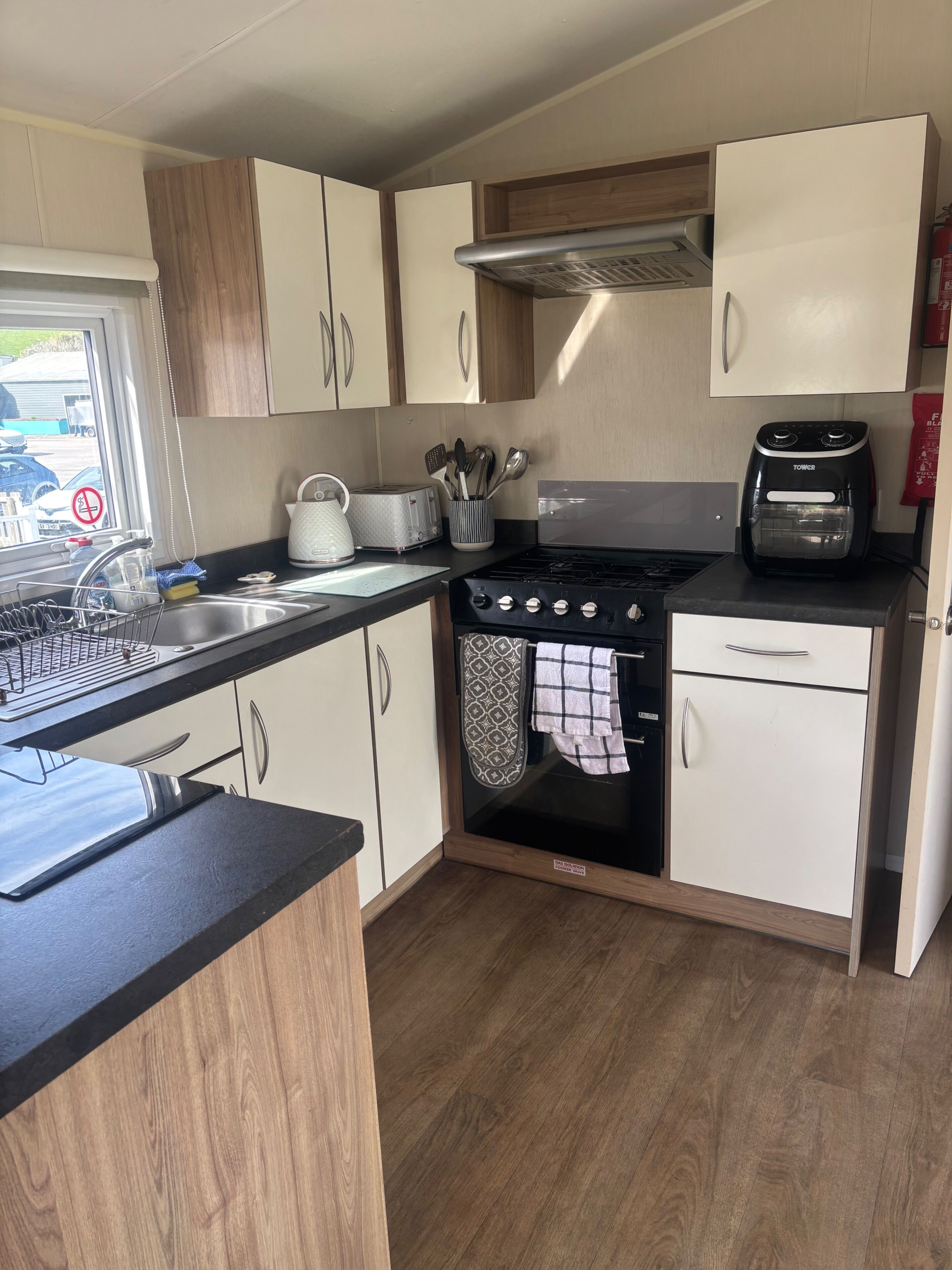 A compact kitchen with a gas stove, toaster, and oven. It features wooden cabinets, a black countertop, and a window with a view of the outside.