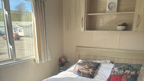 Un lit bien fait, avec des serviettes blanches et roses, une horloge au mur et une fenêtre avec des rideaux.