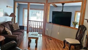 Una sala de estar con piso de madera, un sofá, una mesa de centro, un televisor montado en la pared y un ventilador de techo.