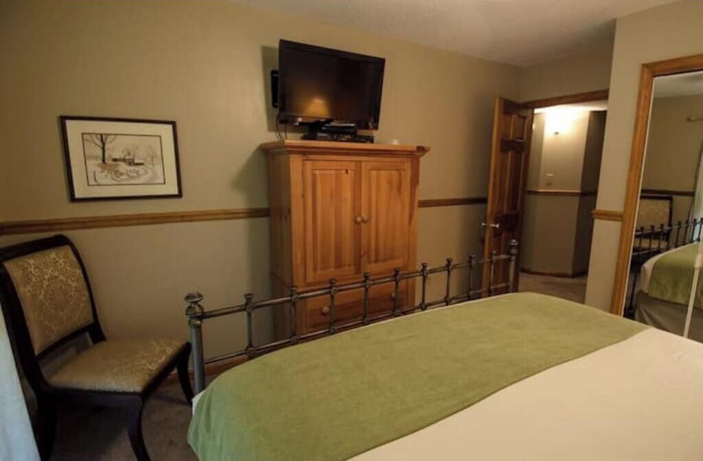 Habitación de hotel con cama, aparador de madera, silla, televisor y un cuadro en la pared.