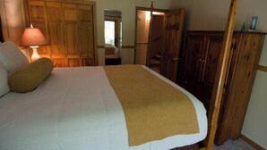 A bedroom with a bed, a wooden wardrobe, and a door leading to another room.