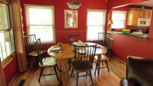 A dining area with a wooden table and chairs, red walls, and a kitchen in the background.