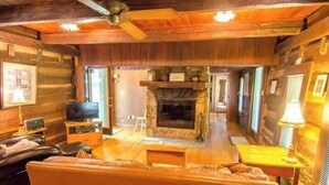 Ein gemütliches Blockhaus-Interieur mit Kamin aus Stein, Holzmöbeln und einem Fernseher.