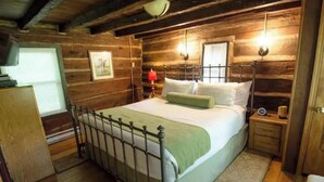 Ein Schlafzimmer einer Holzhütte mit einem Metallbettgestell, einem Nachttisch mit Lampe und einem Fenster mit Jalousien.