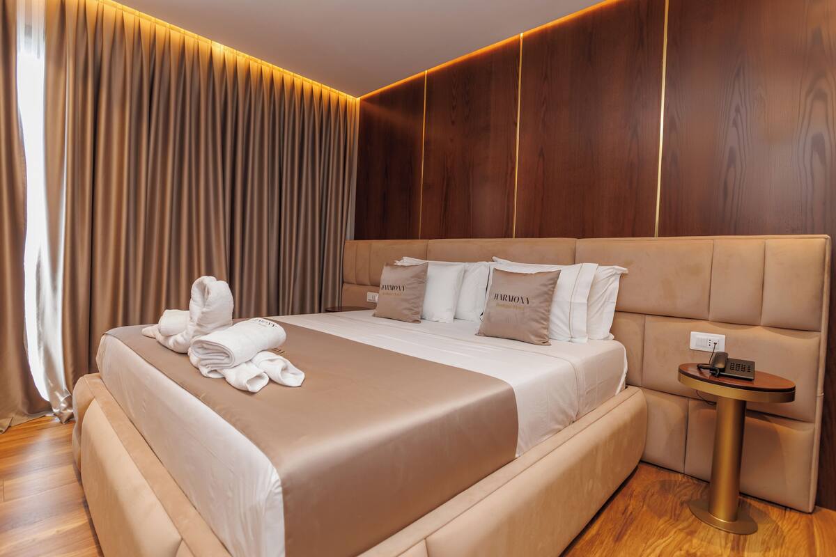 A modern hotel room with a large bed, a bedside table with a phone, and a wooden panel wall.