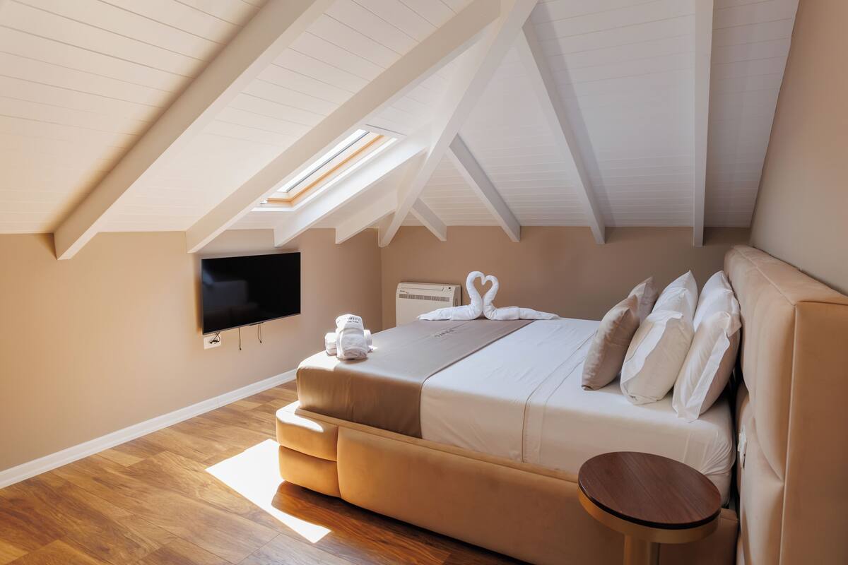 A bedroom with a sloped ceiling, a bed with white bedding, a flat-screen TV, and a small round table.