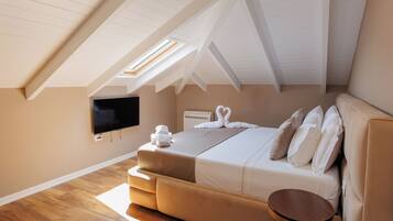 A bedroom with a sloped ceiling, a bed with white bedding, a flat-screen TV, and a small round table.