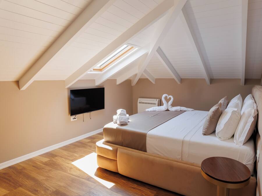A bedroom with a sloped ceiling, a bed with white bedding, a flat-screen TV, and a small round table.