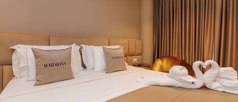 A hotel room with a large bed, two pillows with 'HARMONY Boutique Hotel' text, a bedside table, and a curtain.