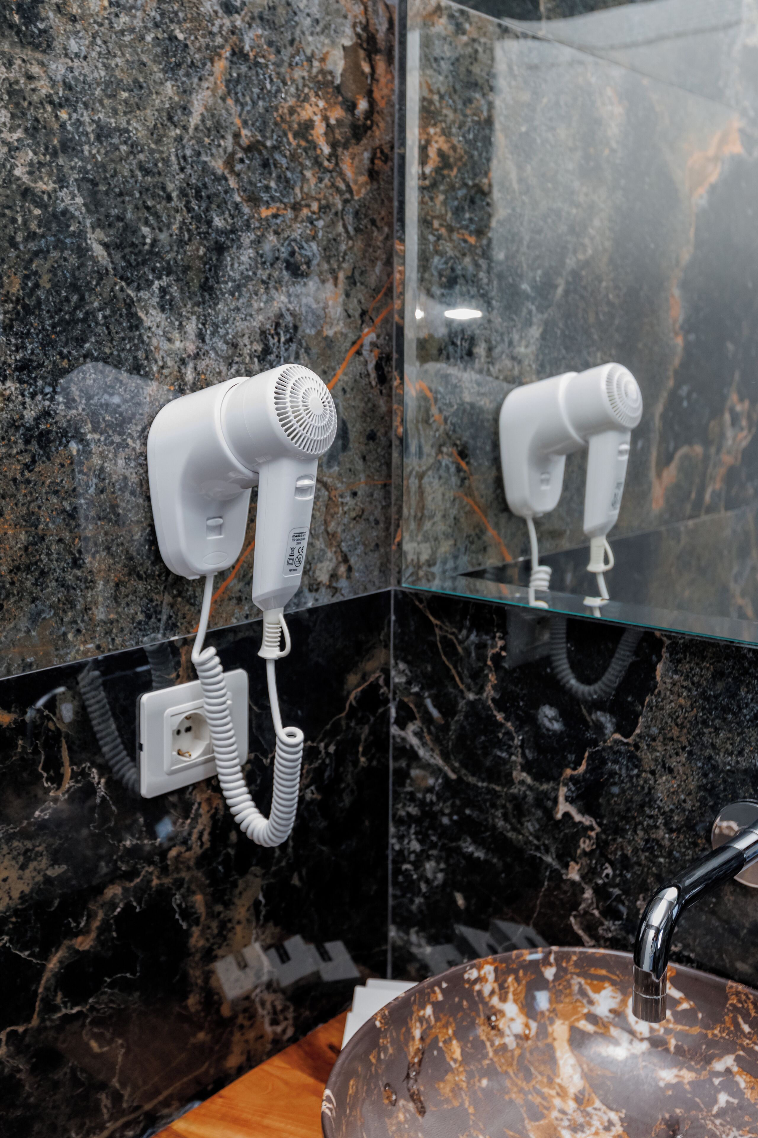 A bathroom with a marble sink, a mirror, and a hairdryer mounted on the wall.