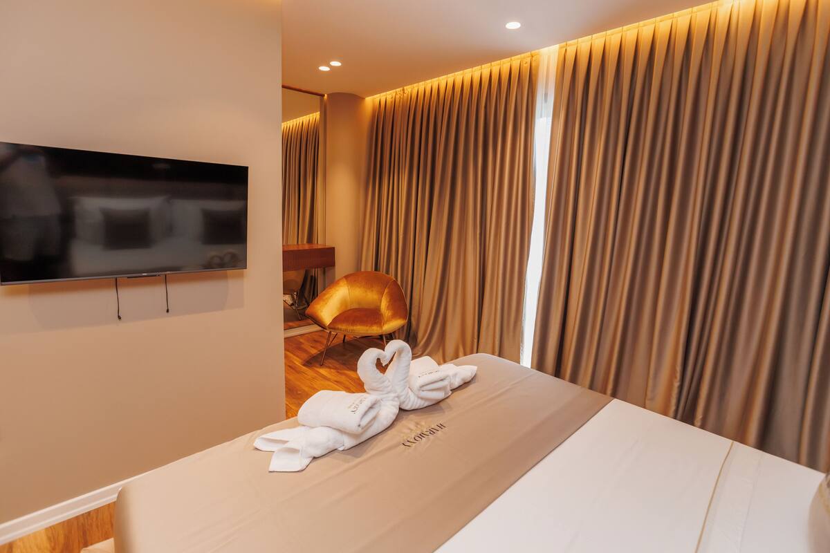 A hotel room with a bed, a flat-screen TV mounted on the wall, and a large window with curtains.