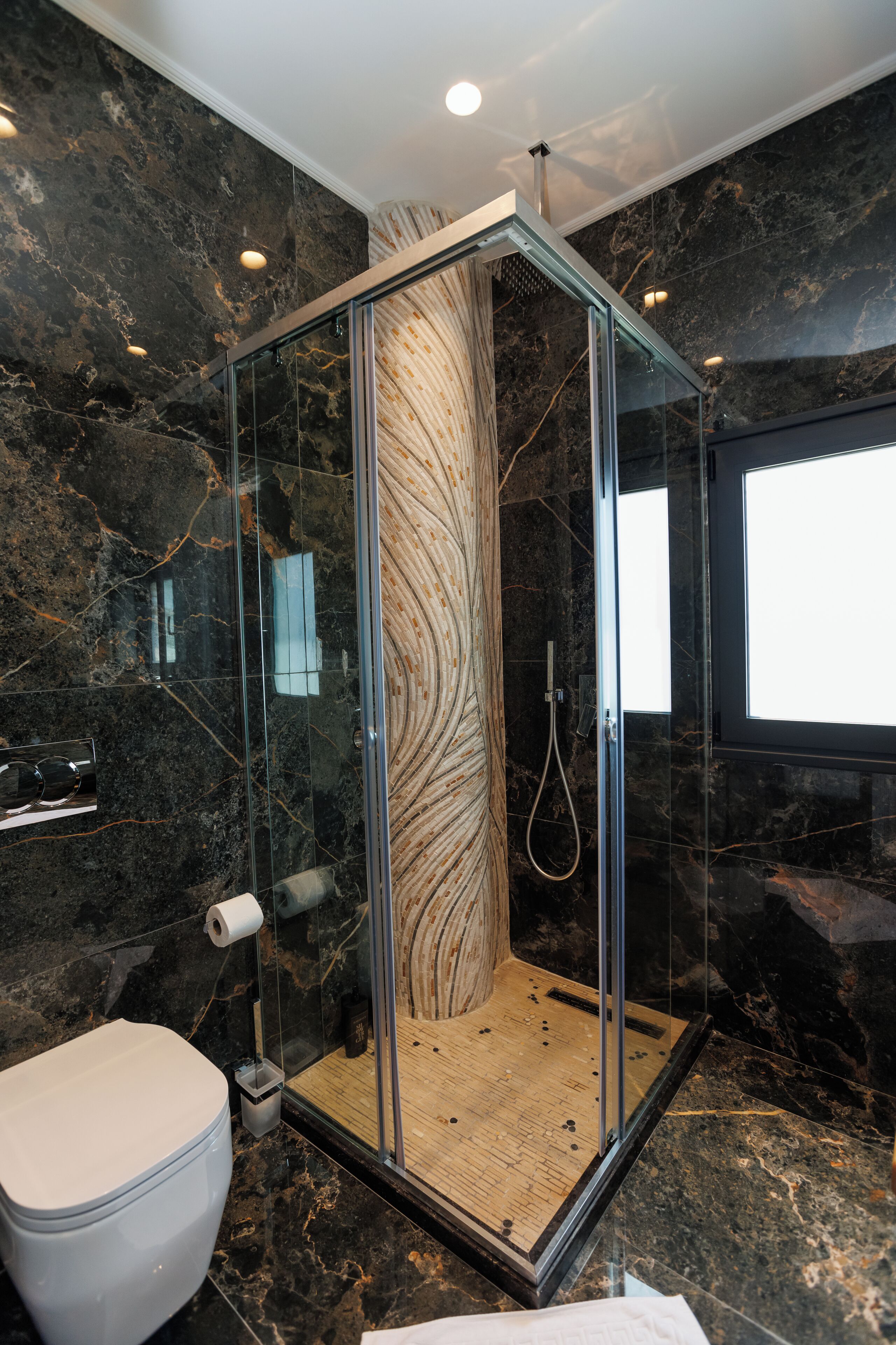 Ein modernes Badezimmer mit einer Duschkabine, Marmorwänden und einer Toilette.
