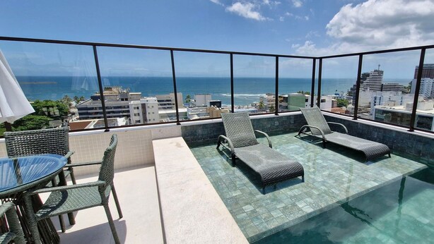 Una piscina infinita en la azotea con sillones de descanso y una mesa, con vistas a la ciudad.