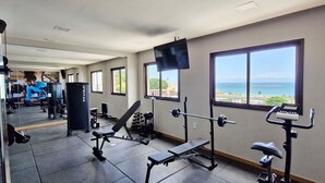 Un gimnasio con equipo de ejercicio, una banca y vistas al mar a través de amplios ventanales.