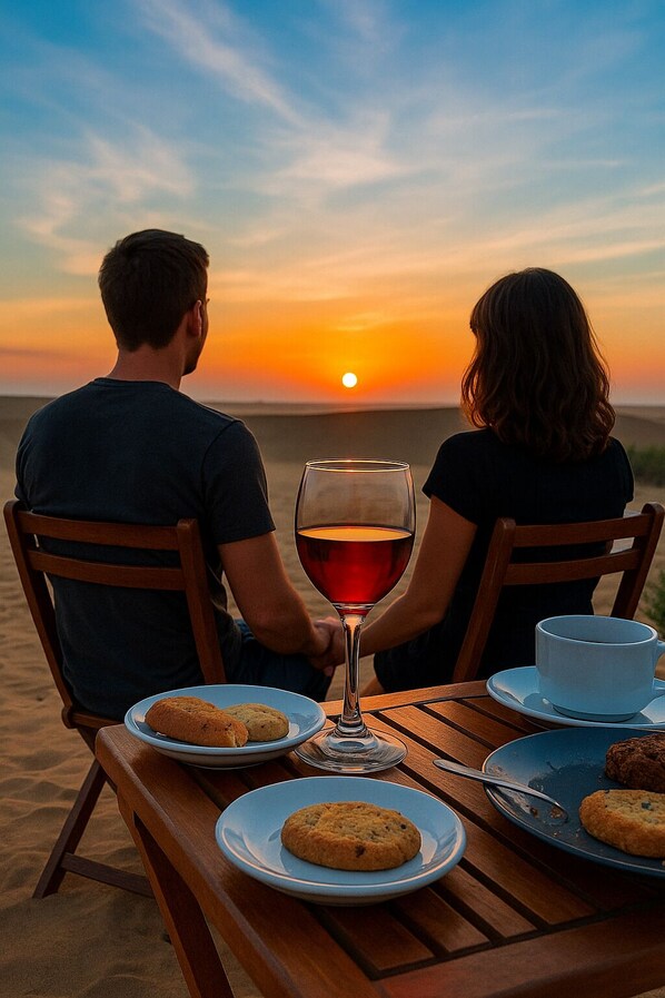 Una pareja sentada en una mesa de madera en la playa, mirando la puesta de sol.