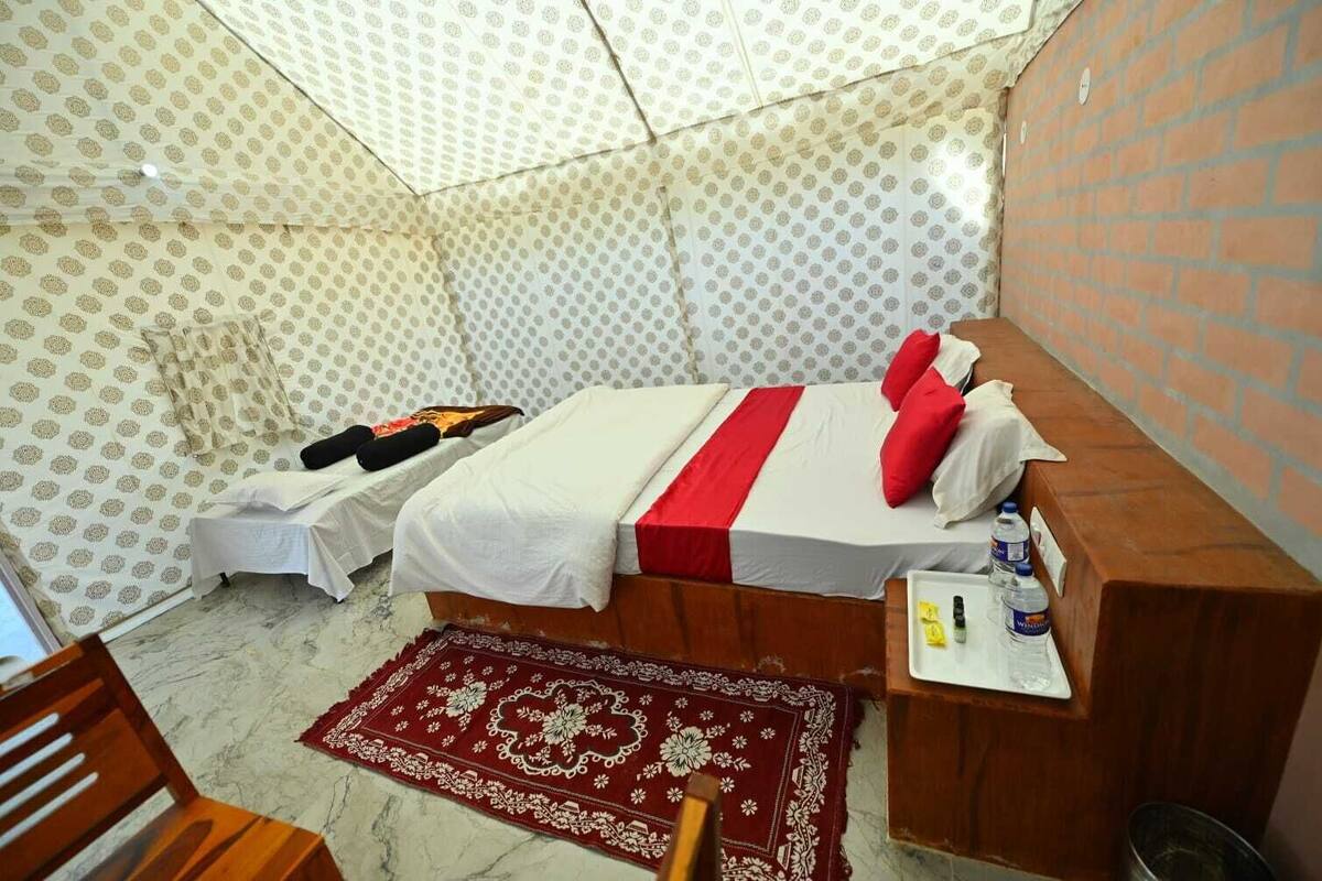 A room with a bed, a small table with toiletries, a red patterned rug, and a wooden chair.
