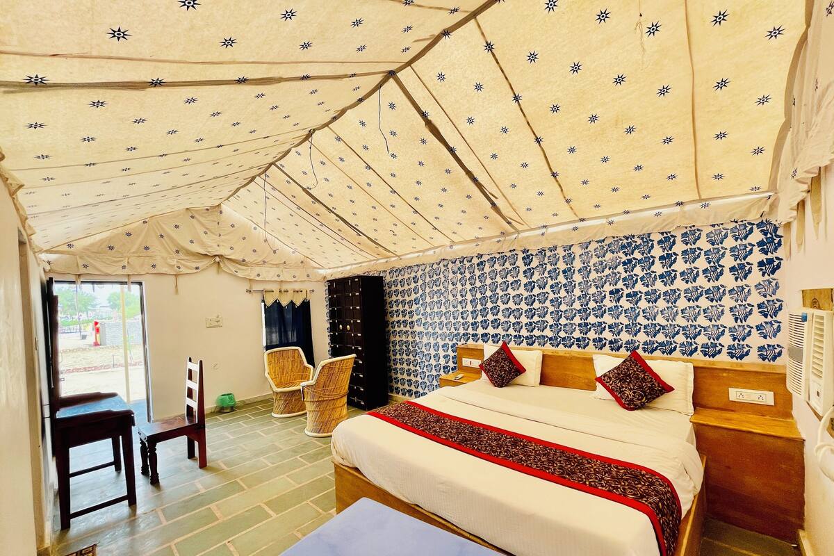 A tented room with a bed, two chairs, a small table, and a wall with a blue floral pattern.