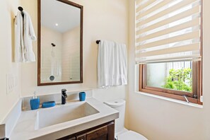 Une salle de bain équipée d’un lavabo, d’un miroir, de toilettes et d’une fenêtre avec des stores.