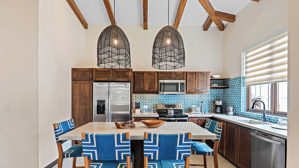A modern kitchen with wooden cabinets, a stainless steel refrigerator, a microwave, and a blue tiled backsplash. - Stylish Condo in the Heart of Las Catalinas with Vibrant Design & Exclusive Beach Club Access (Las Catalinas)