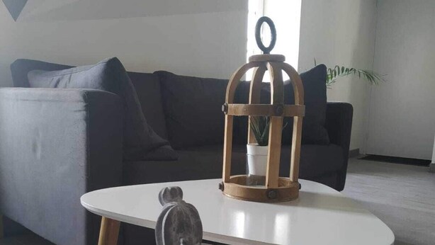 Moderni olohuone, jossa on valkoinen pyöreä pöytä, harmaa veistos ja puinen kukkaruukku, jossa on kasvi.