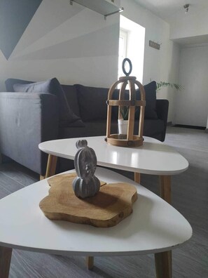 Un salón moderno con una mesa redonda blanca, una escultura gris y una jardinera de madera con una planta.