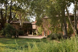 A traditional stone building with a courtyard, surrounded by mature trees and a well-maintained lawn. - Château de Sienne (Chusclan)
