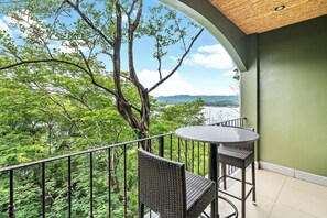 A balcony with a round table and two wicker chairs, overlooking a lush green landscape and a body of water. - Luxury Condo with Panoramic Ocean Views, Sparkling Infinity Pool, and Modern Open-Concept Design (Cabo Velas)