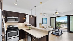A modern kitchen with dark wood cabinets, stainless steel appliances, and pendant lighting. - Luxury Condo with Panoramic Ocean Views, Sparkling Infinity Pool, and Modern Open-Concept Design (Cabo Velas)