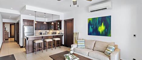 A modern kitchen with dark wooden cabinets, a central island with bar stools, a ceiling fan, and an air conditioning unit.