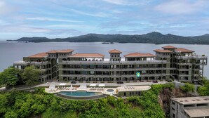 A large hotel with multiple balconies overlooking a body of water and mountains. - Luxury Condo with Panoramic Ocean Views, Sparkling Infinity Pool, and Modern Open-Concept Design (Cabo Velas)