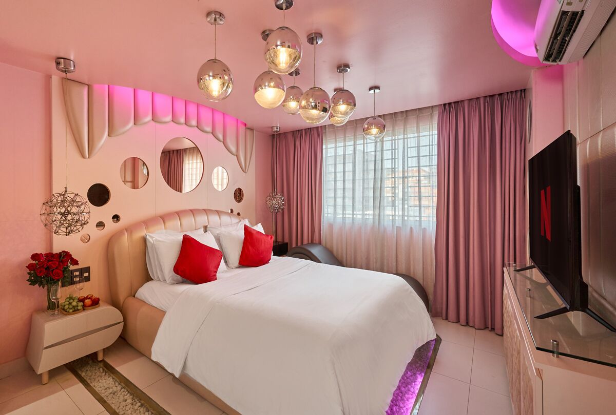 A modern bedroom with a large bed, pink curtains, and a TV on a glass cabinet.