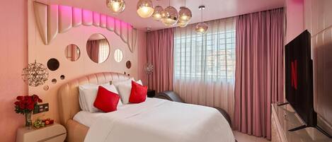 A modern bedroom with a large bed, pink curtains, and a TV on a glass cabinet.