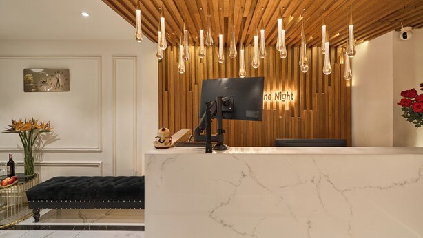 A reception desk with a wooden panel background, a flat-screen TV, and a sign that reads "ne Night". - Secret Garden Hotel Ben Thanh (Ho Chi Minh City)