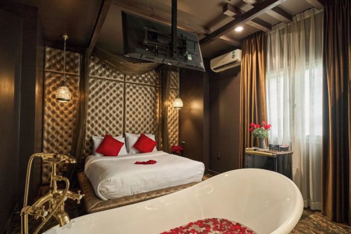 A luxurious bedroom with a large white bathtub, a classic bed with red pillows, and a decorative wall panel.