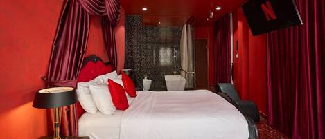 A hotel room with a large bed, a bedside table, a TV, and a bathroom with a shower and toilet.