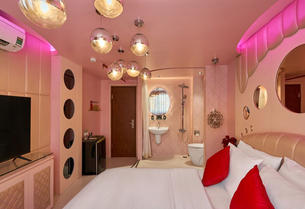 Un dormitorio con televisor, cama con almohadas rojas, tocador con espejo y ducha.