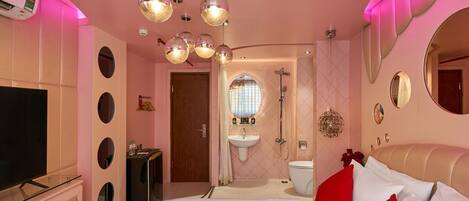 Un dormitorio con televisor, cama con almohadas rojas, tocador con espejo y ducha.